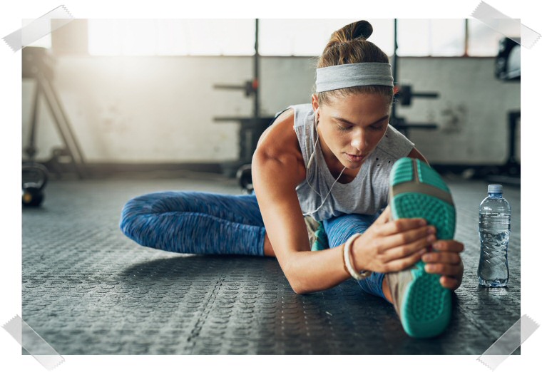 Picture of a young woman stretching her body towards the feet. Next to her is a water bottle.